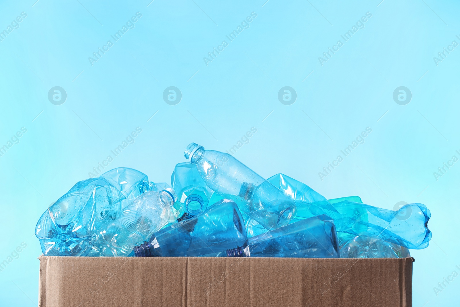 Photo of Cardboard box with used plastic bottles and space for text on color background. Recycling problem