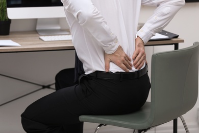 Photo of Businessman suffering from back pain at workplace, closeup