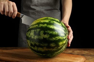 Photo of Woman cutting delicious watermelon at wooden table against black background, closeup