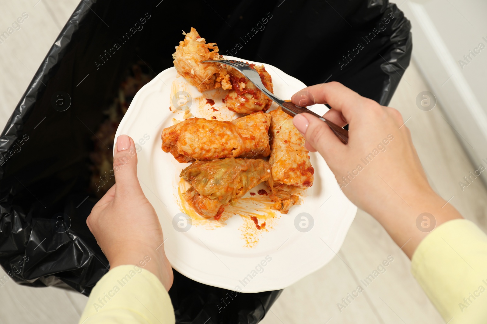 Photo of Woman throwing cabbage rolls into bin indoors, top view