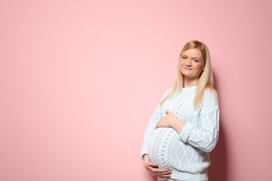 Beautiful pregnant woman in sweater on color background. Space for text