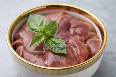 Bowl with raw chicken liver and basil on light grey table, closeup