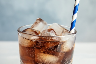 Glass of refreshing soda drink with ice cubes and straw on blue background, closeup