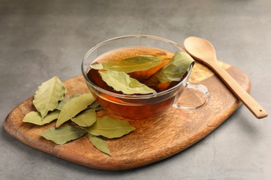 Photo of Cup of freshly brewed tea with bay leaves on grey table