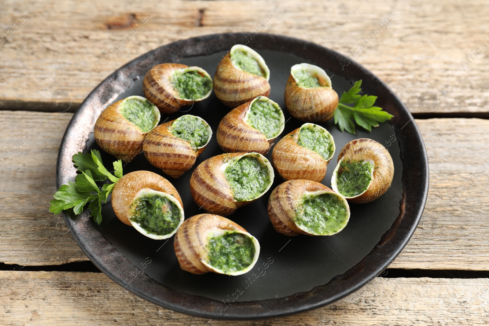 Photo of Delicious cooked snails with parsley on wooden table