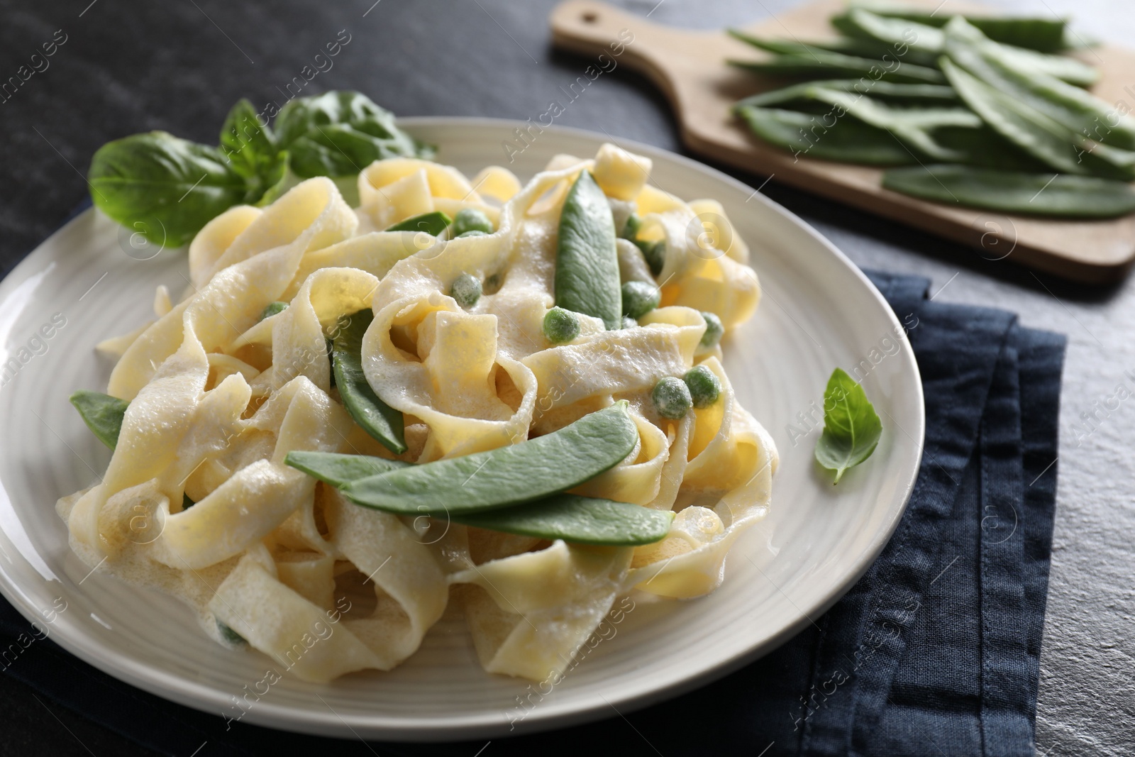 Photo of Delicious pasta with green peas and creamy sauce on black table