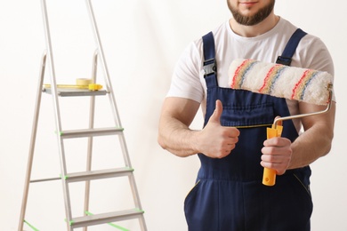 Photo of Male decorator with paint roller in empty room, closeup. Space for text