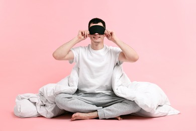 Photo of Happy man in pyjama with sleep mask and blanket on pink background