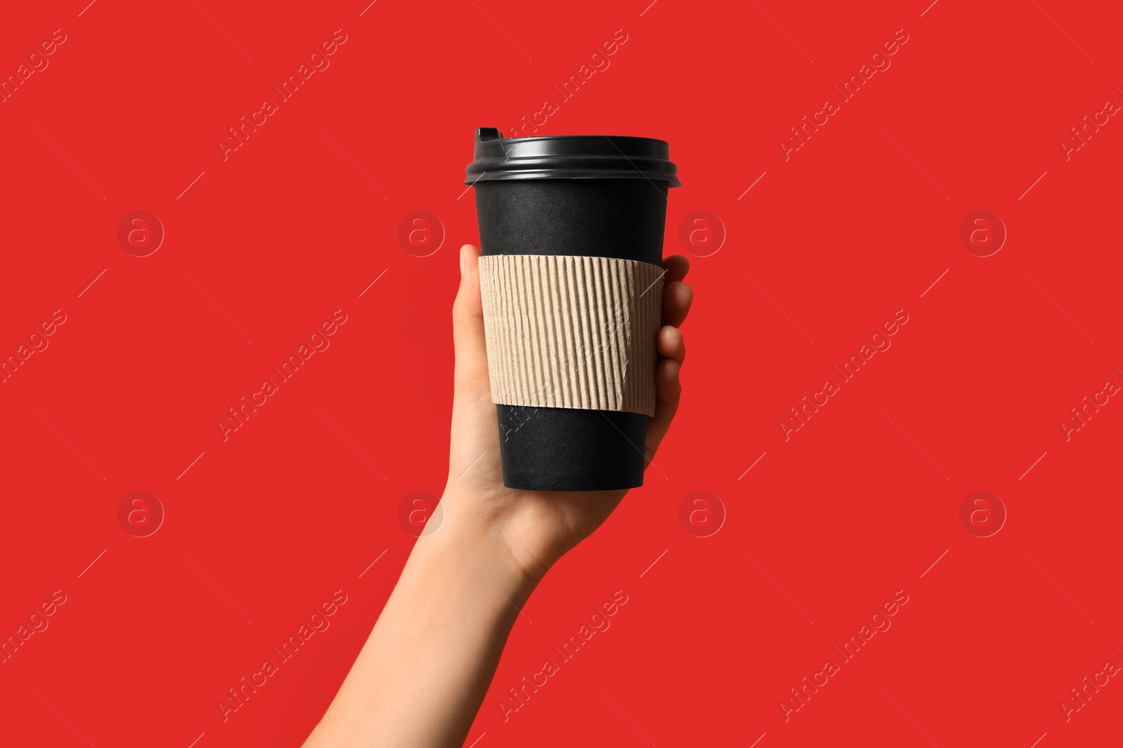 Photo of Woman holding takeaway paper coffee cup with cardboard sleeve on red background, closeup