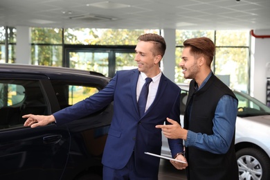 Photo of Young car salesman working with client in dealership