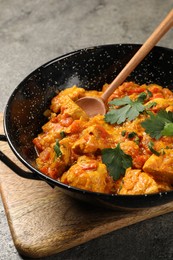 Delicious chicken curry in frying pan and spoon on grey table