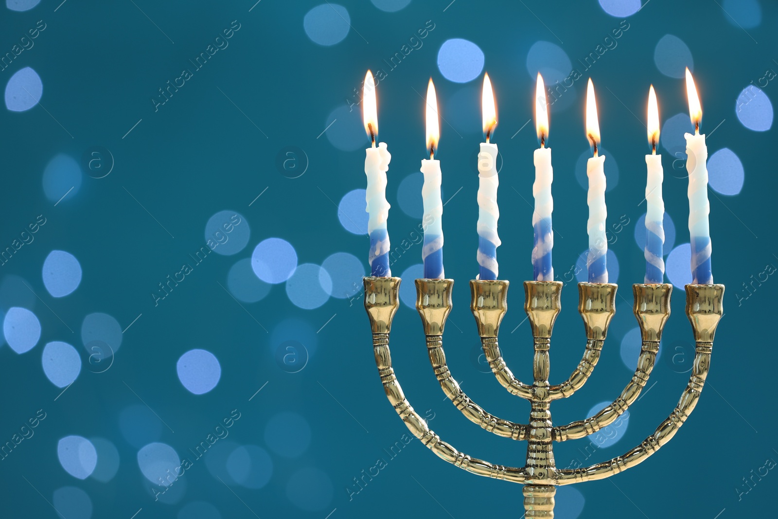 Photo of Hanukkah celebration. Menorah with burning candles on blue background with blurred lights, space for text