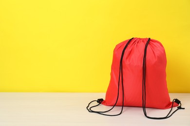 Photo of Red drawstring bag on white wooden table against yellow background. Space for text