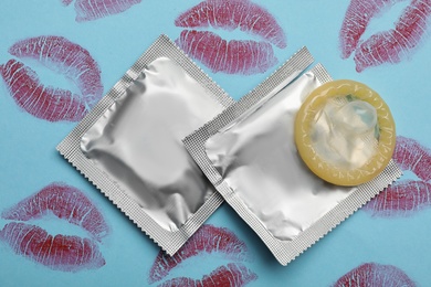 Photo of Condoms with lipstick kiss marks on light blue background, flat lay. Safe sex