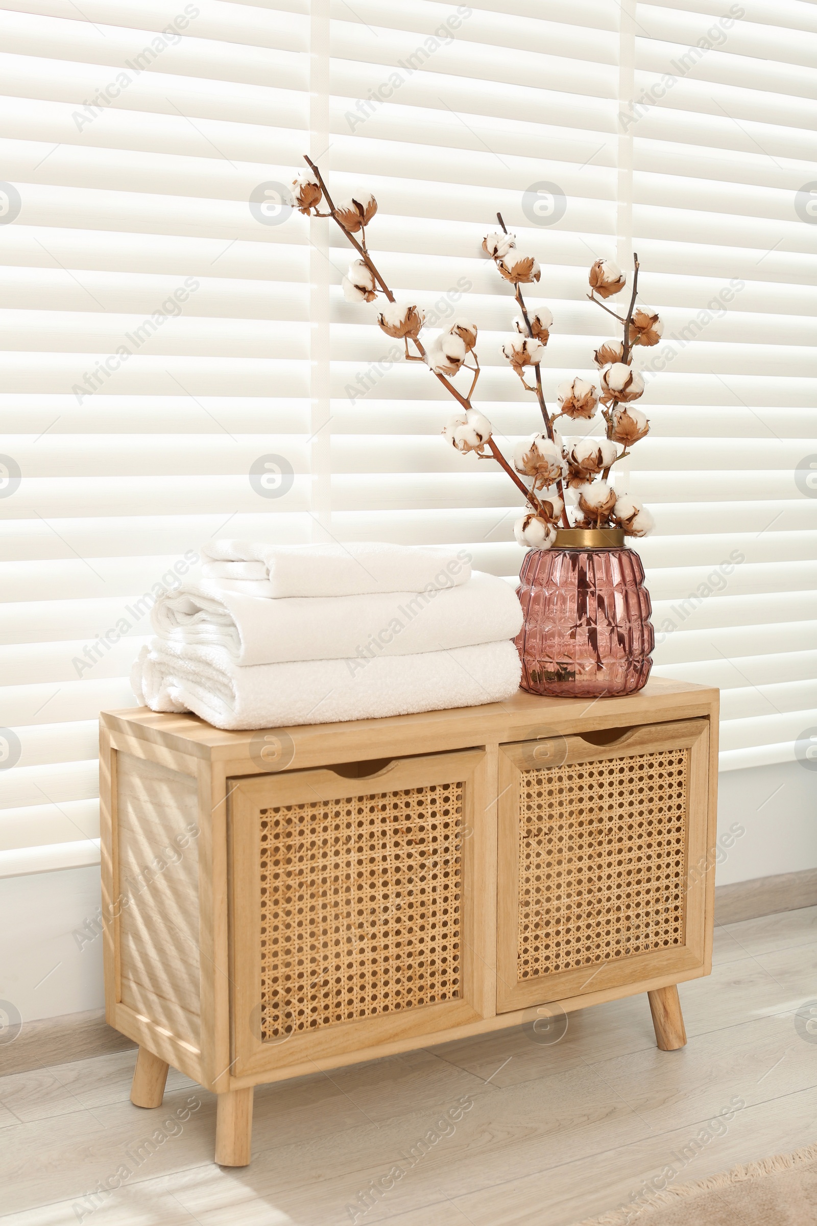 Photo of Soft towels and vase with cotton branches on wooden cabinet in bathroom