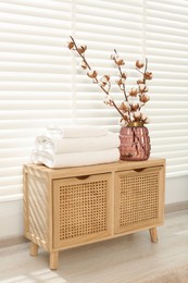 Photo of Soft towels and vase with cotton branches on wooden cabinet in bathroom