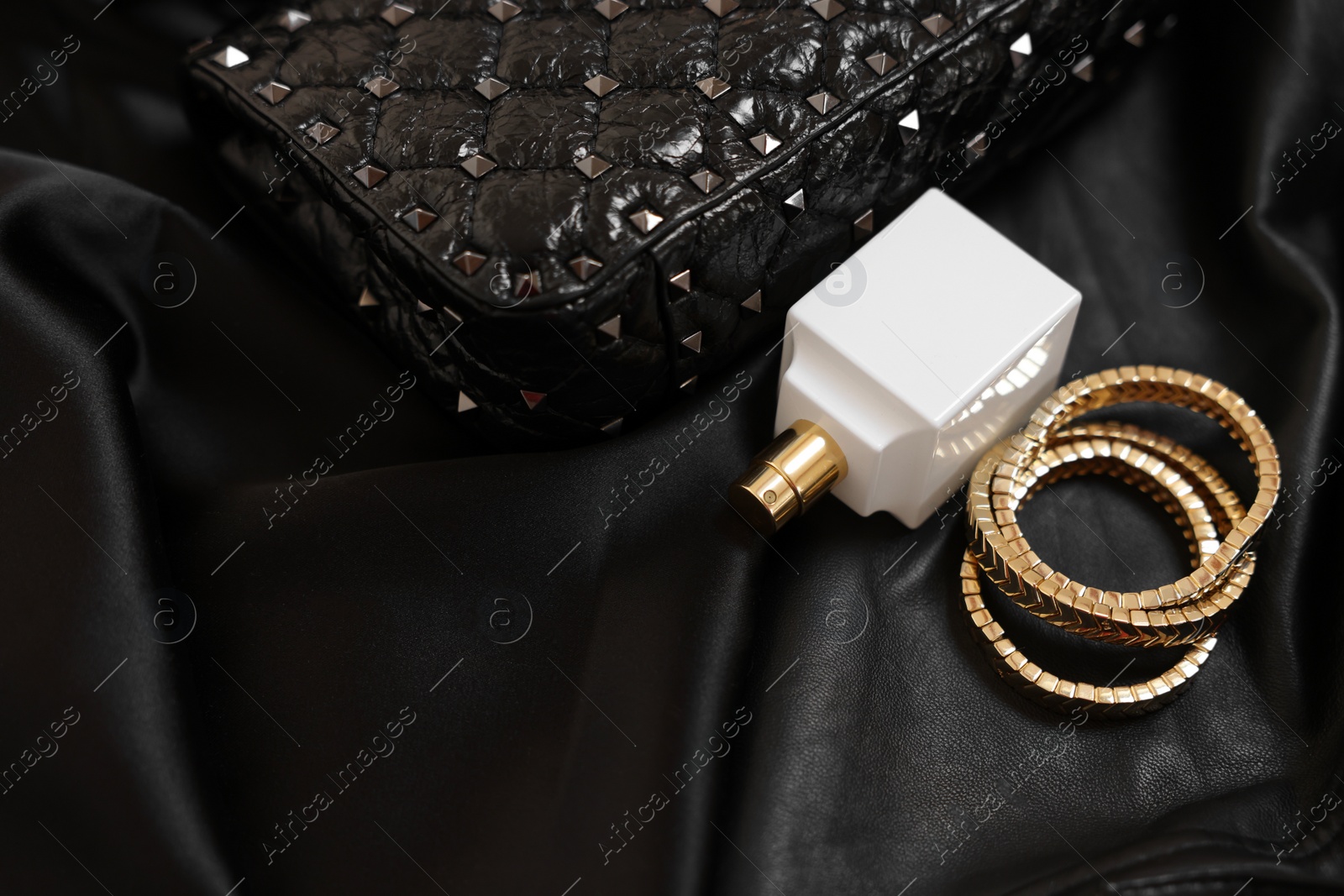 Photo of Leather bag, bottle of perfume and golden bracelets on black fabric, closeup. Space for text