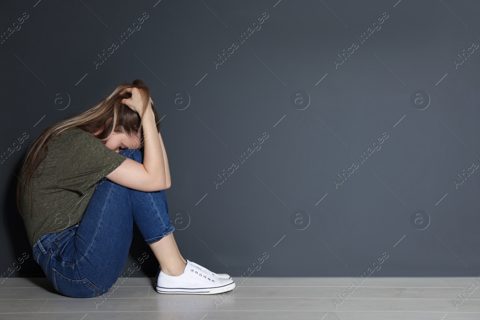 Photo of Upset young woman sitting on floor near grey wall. Space for text