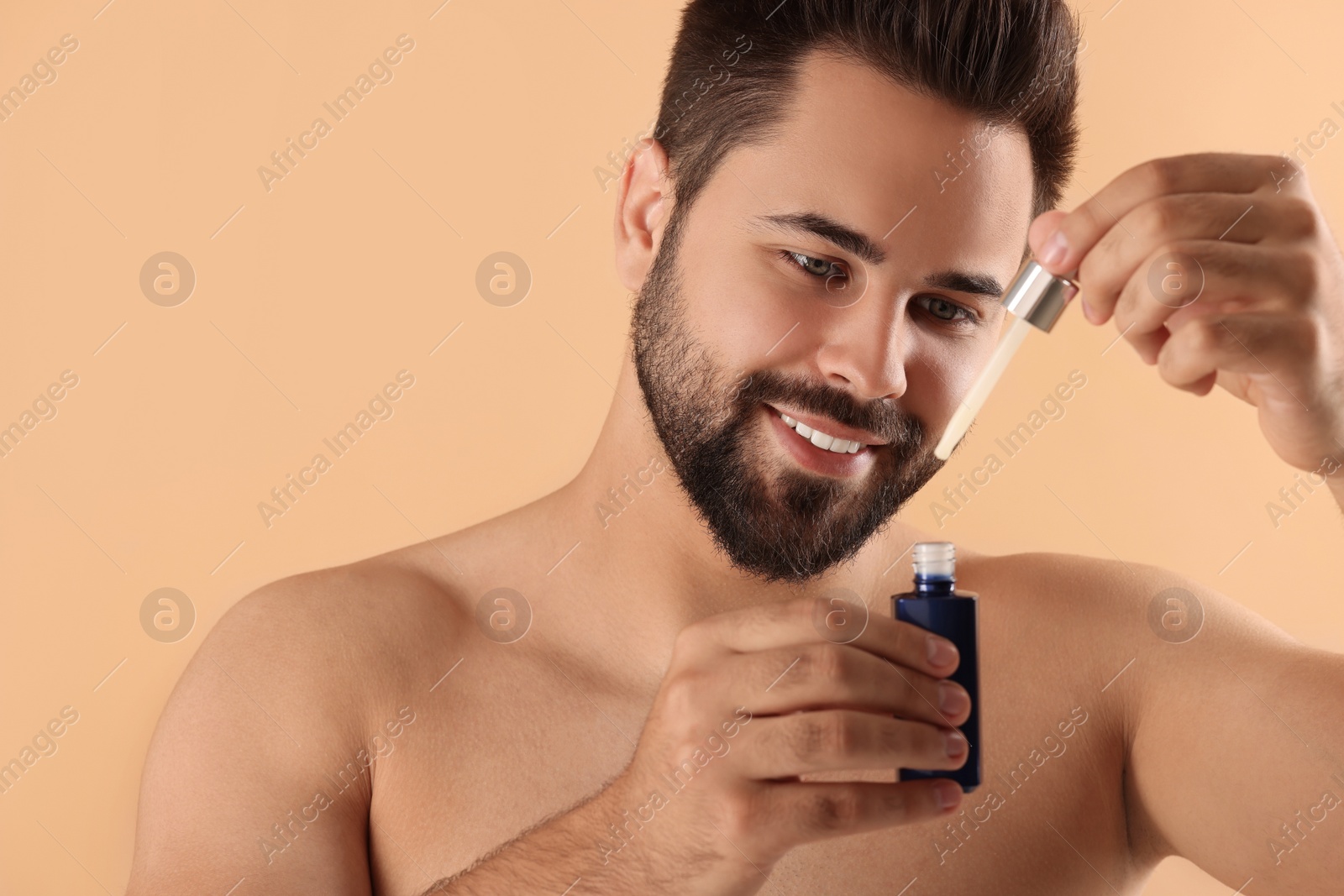 Photo of Handsome man with cosmetic serum in hands on beige background