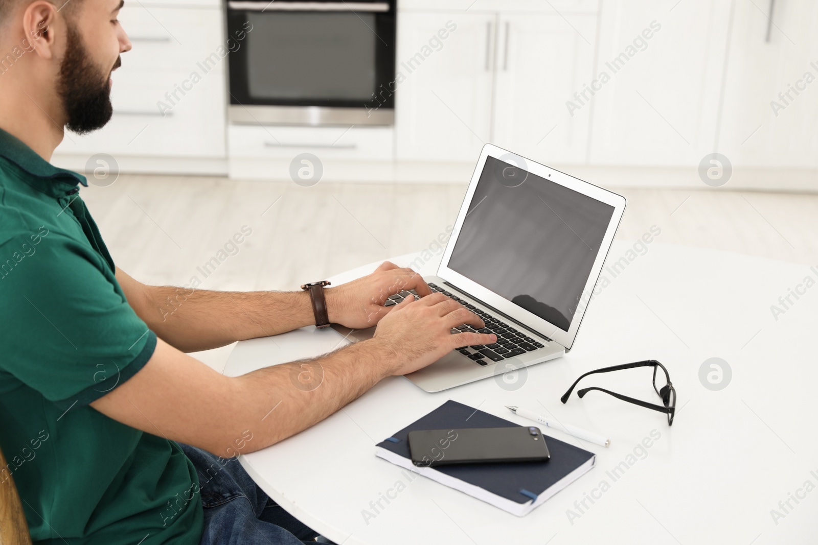 Photo of Handsome young man working with laptop at table in kitchen