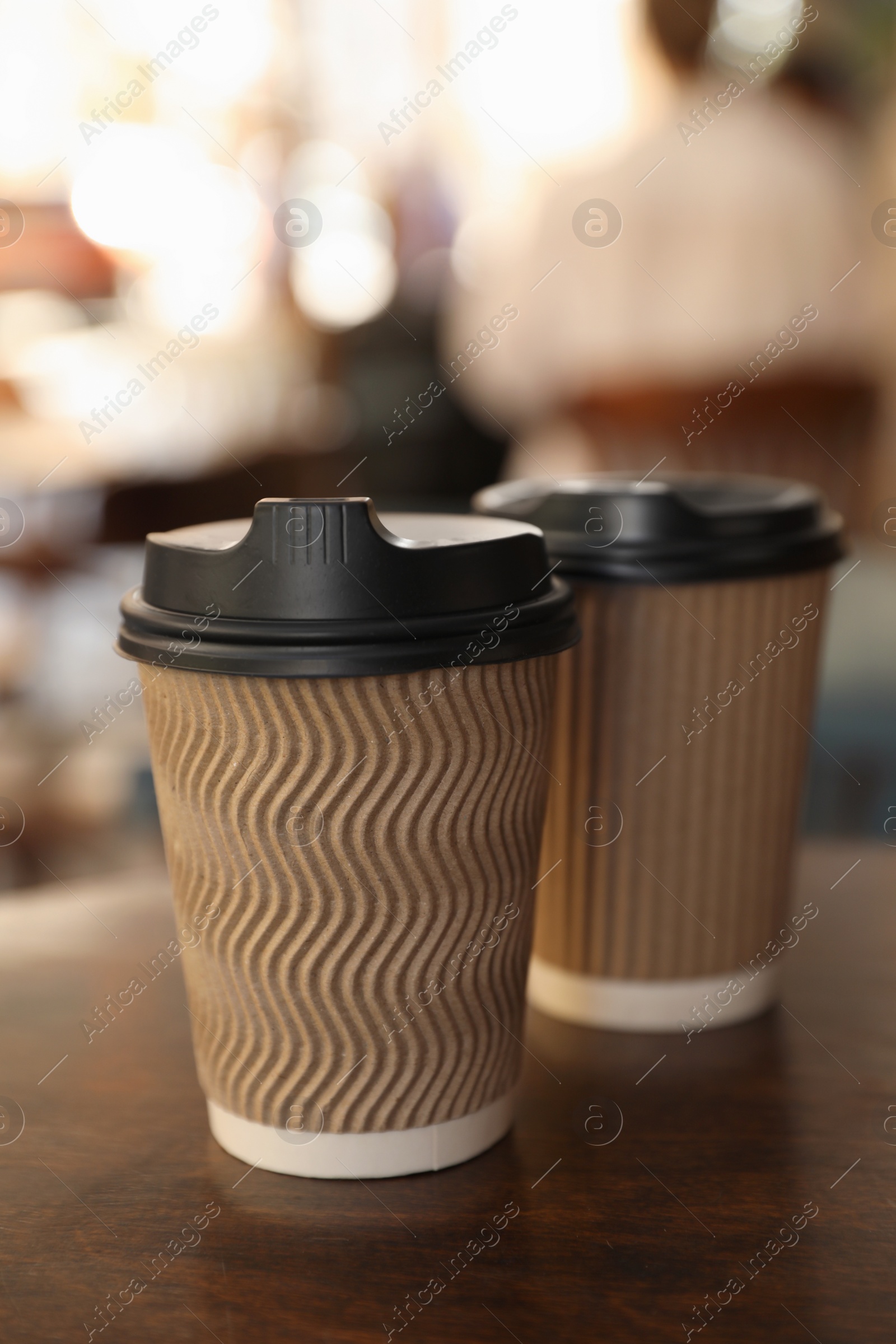 Photo of Cardboard takeaway coffee cups with plastic lids on wooden table in city