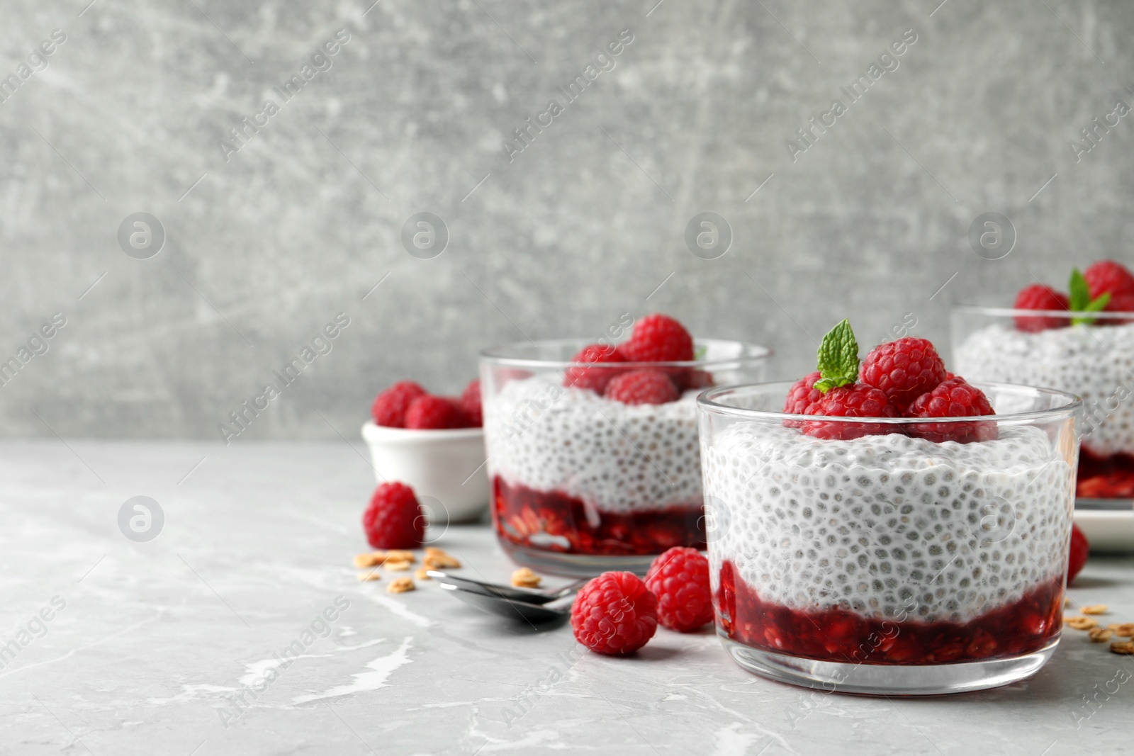Photo of Delicious chia pudding with raspberries and mint on light marble table, space for text