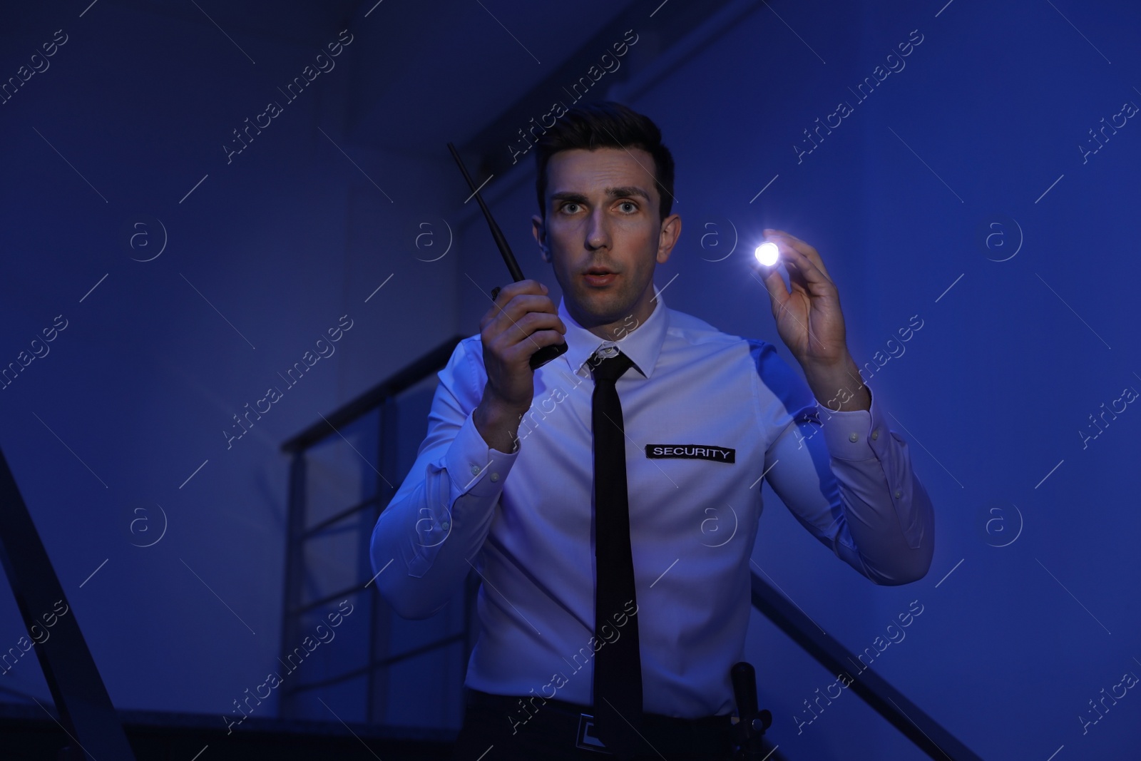 Photo of Male security guard with flashlight and portable radio transmitter in dark room