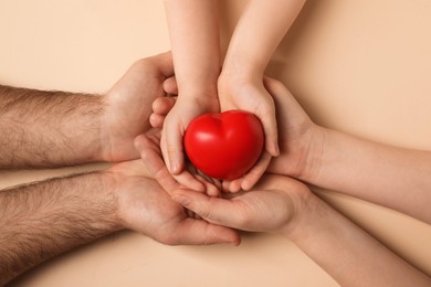 Parents and kid holding red heart in hands on beige background, top view