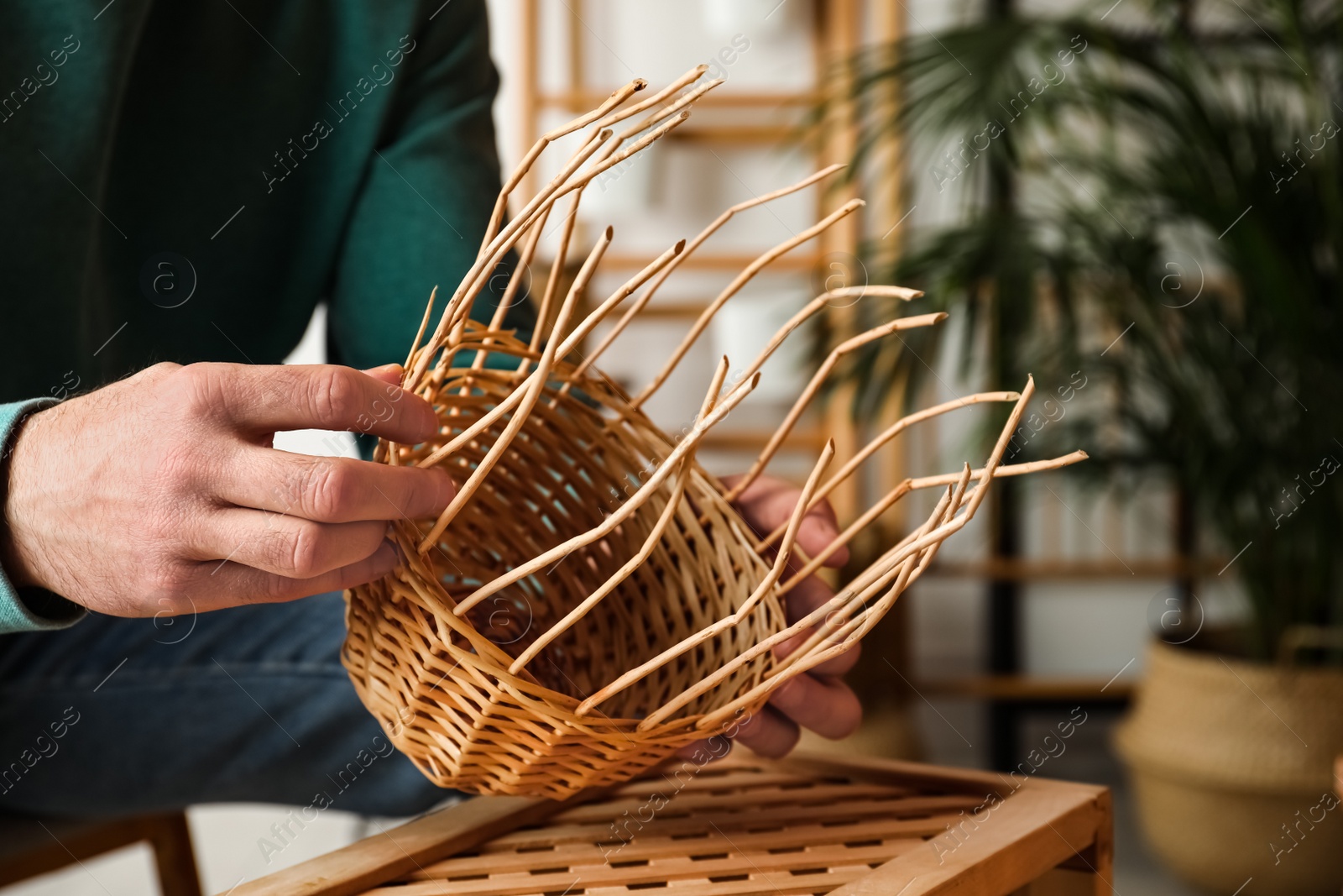 Photo of Man weaving wicker basket indoors, closeup view