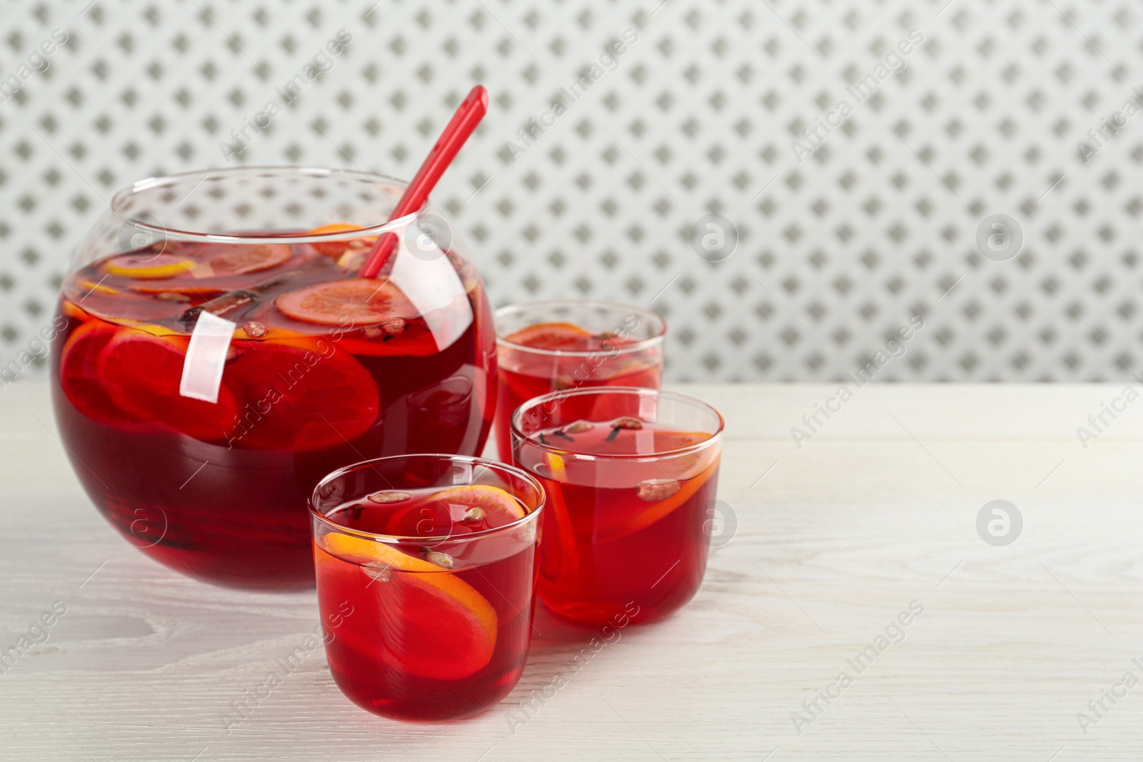 Photo of Glasses and bowl of delicious aromatic punch drink on white wooden table. Space for text