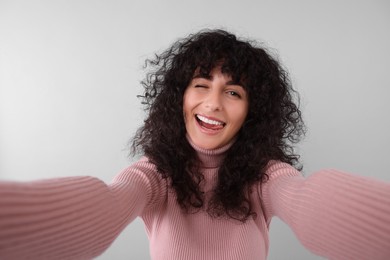 Beautiful young woman taking selfie on light grey background