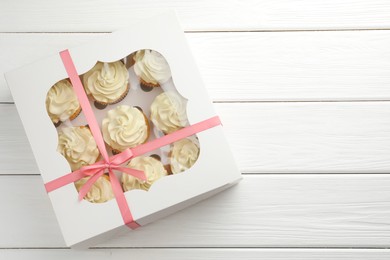 Photo of Tasty cupcakes with vanilla cream in box on white wooden table, top view. Space for text