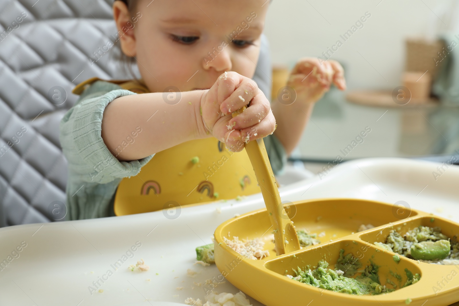 Photo of Little baby eating healthy food in high chair indoors, closeup