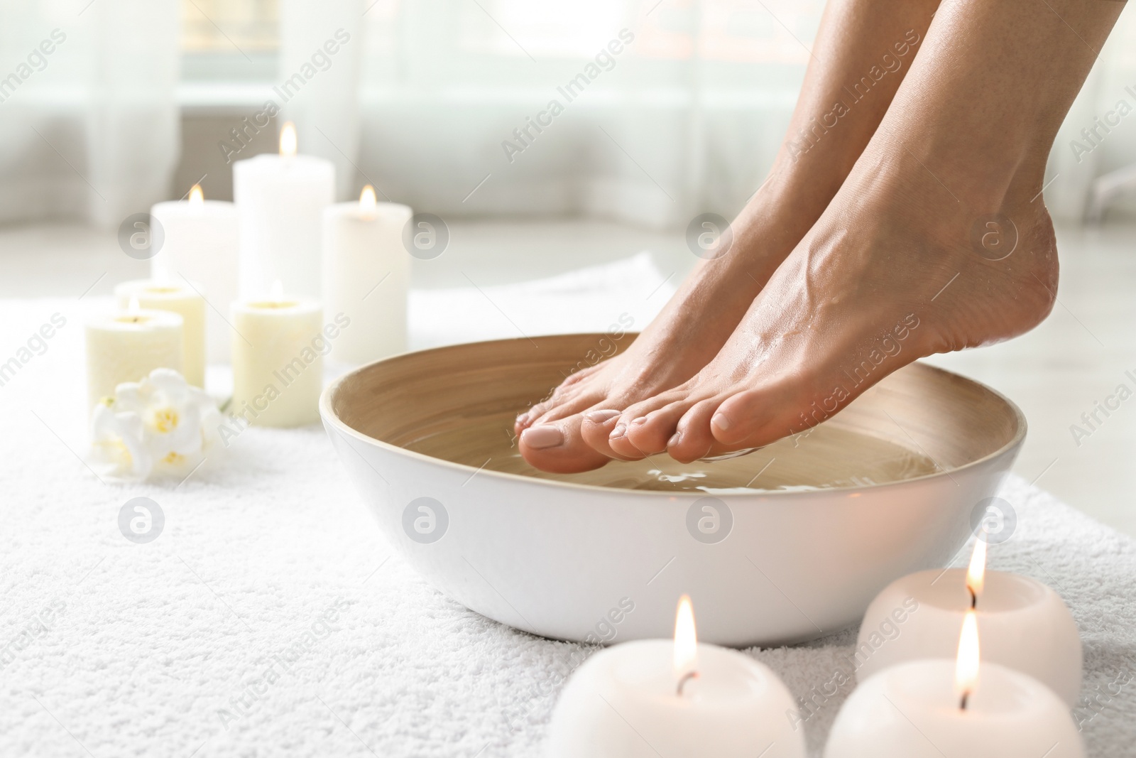 Photo of Woman soaking her feet in dish indoors, closeup with space for text. Spa treatment
