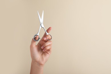 Photo of Hairdresser holding professional scissors and space for text on beige background, closeup. Haircut tool