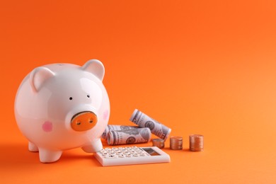 Financial savings. Piggy bank, dollar banknotes, coins and calculator on orange background