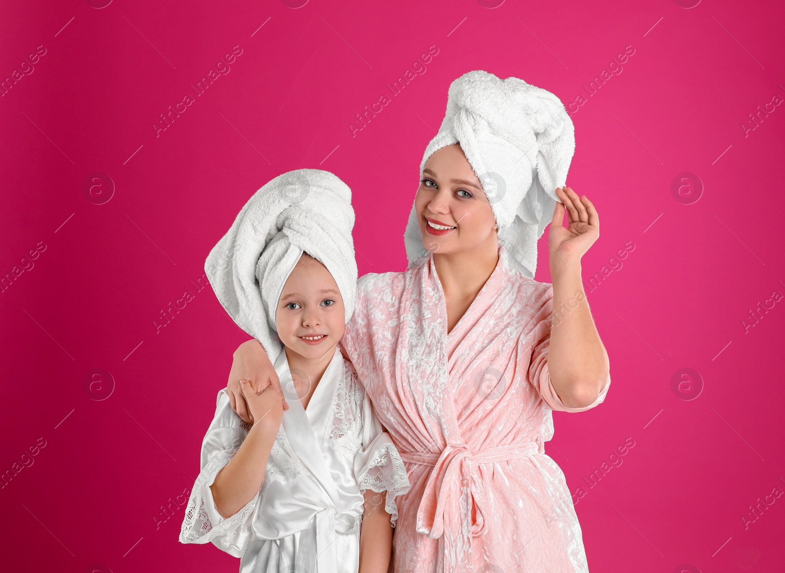 Photo of Happy mother and little daughter wearing bathrobes on pink background