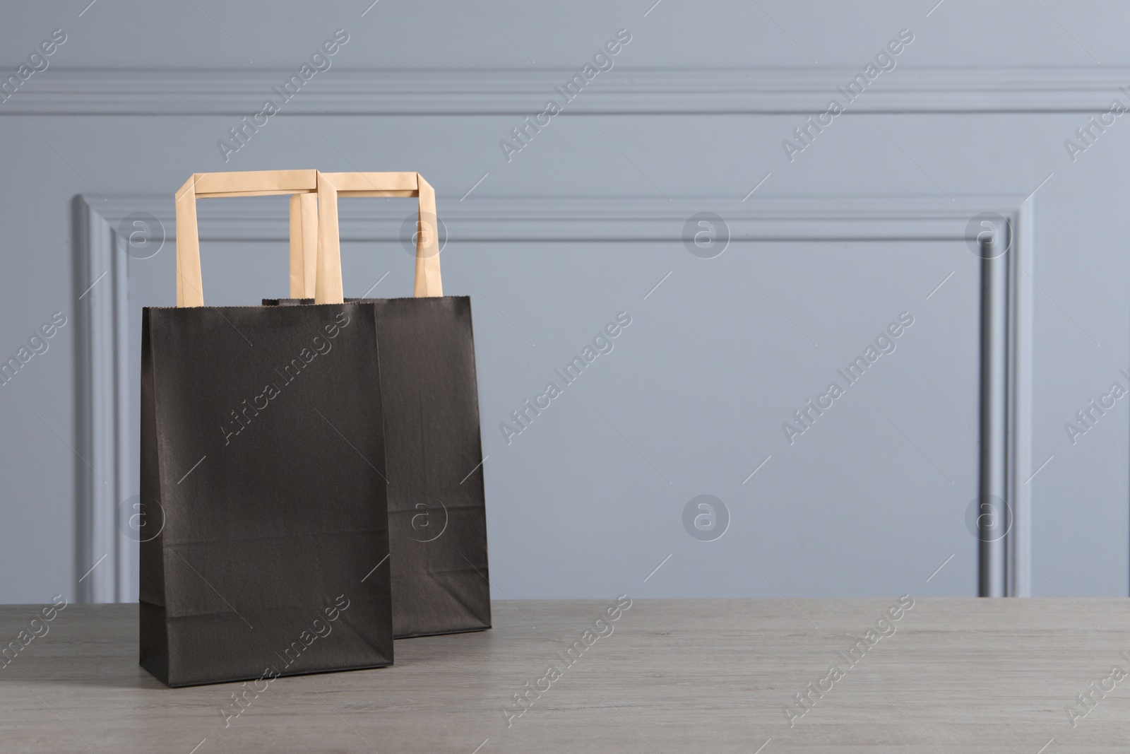 Photo of Black paper bags on wooden table against light grey wall, space for text