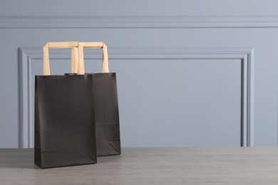 Photo of Black paper bags on wooden table against light grey wall, space for text