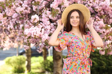 Photo of Beautiful woman in straw hat near blossoming tree on spring day