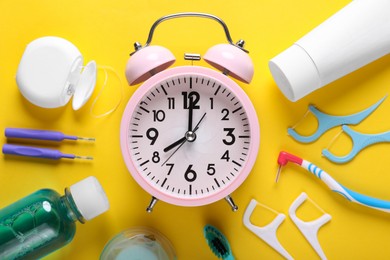 Photo of Dental floss, different teeth care products and alarm clock on yellow background, flat lay