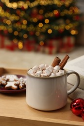Photo of Christmas cocoa with marshmallows and cinnamon sticks in grey cup on wooden tray indoors, closeup. Space for text