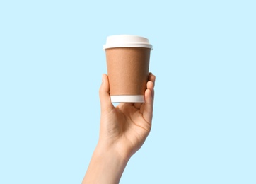 Woman holding takeaway paper coffee cup on light blue background, closeup
