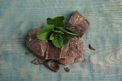 Photo of Tasty dark chocolate pieces with mint on blue wooden table, flat lay