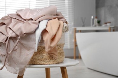 Photo of Wicker laundry basket with clothes on stool in bathroom, closeup