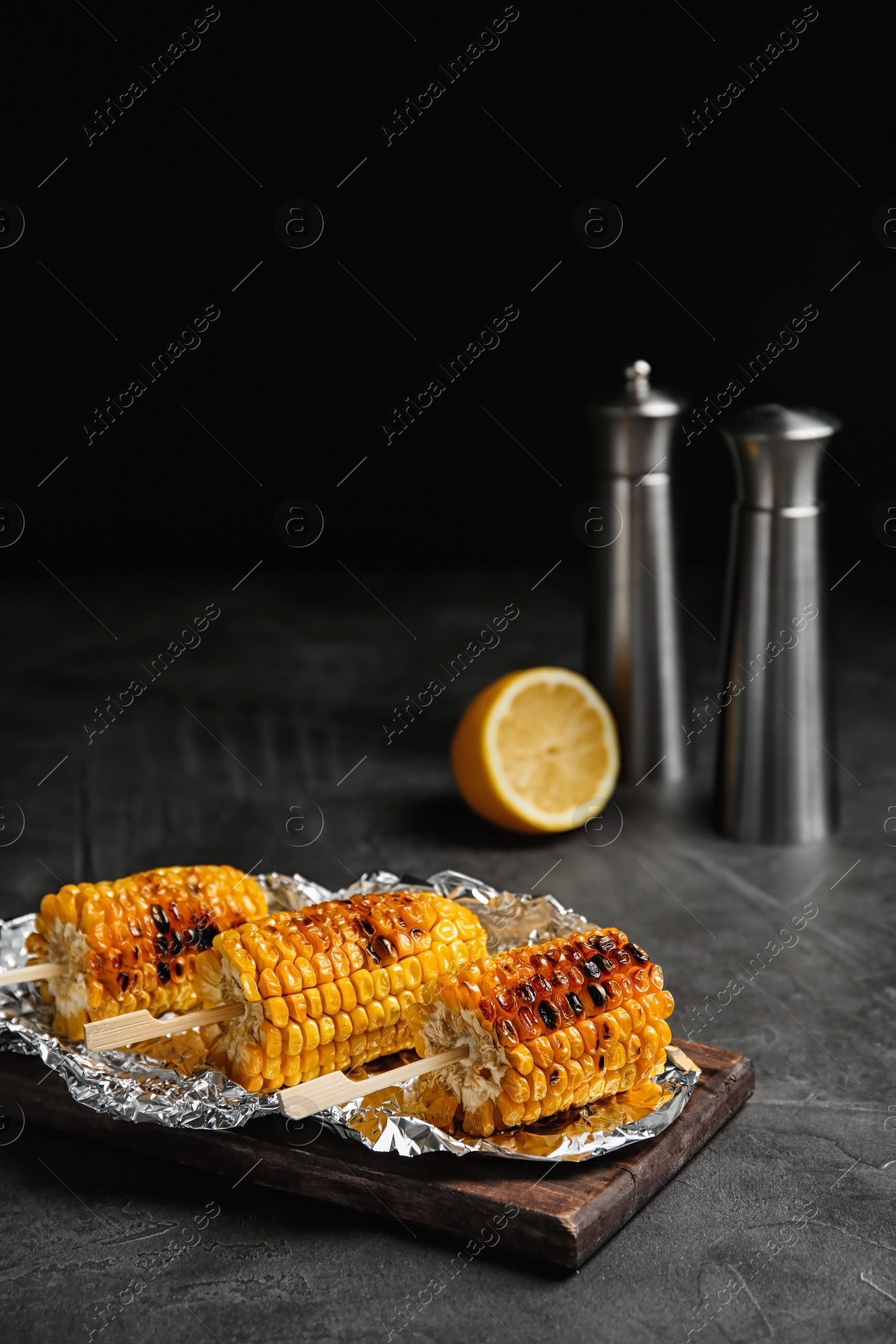 Photo of Delicious grilled corn cobs on table against black background. Space for text