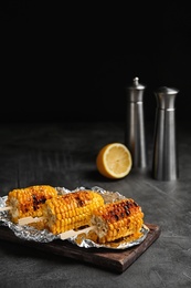 Delicious grilled corn cobs on table against black background. Space for text