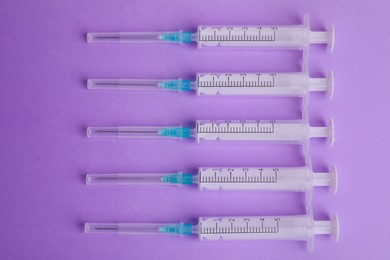 Disposable syringes with needles on violet background, flat lay