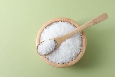 Photo of Organic white salt in bowl and spoon on olive background, top view