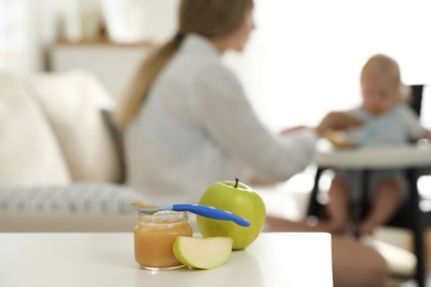 Photo of Mother feeding her little baby at home, focus on healthy fruit puree and fresh apples